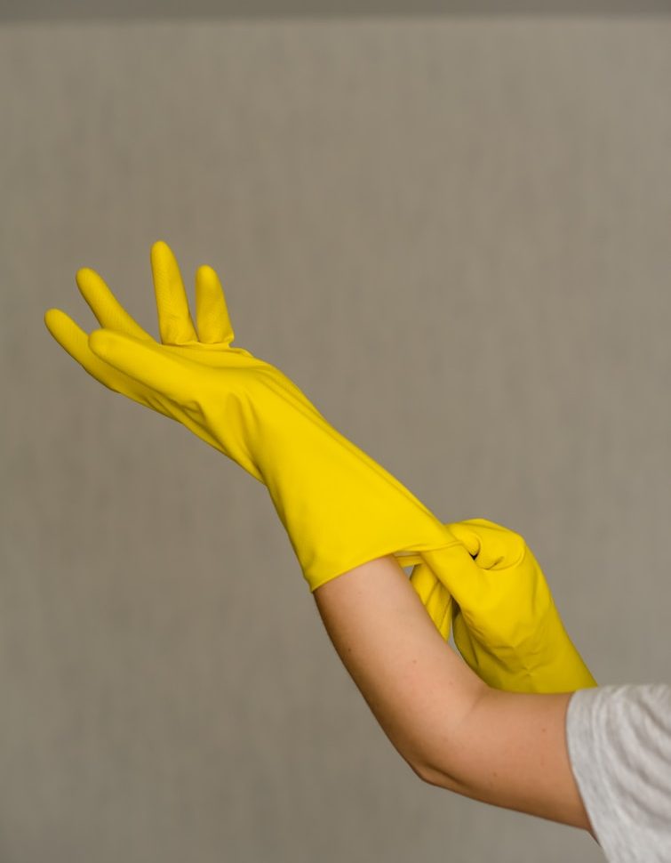 Eine Hand zieht gelbe Gummihandschuhe an.