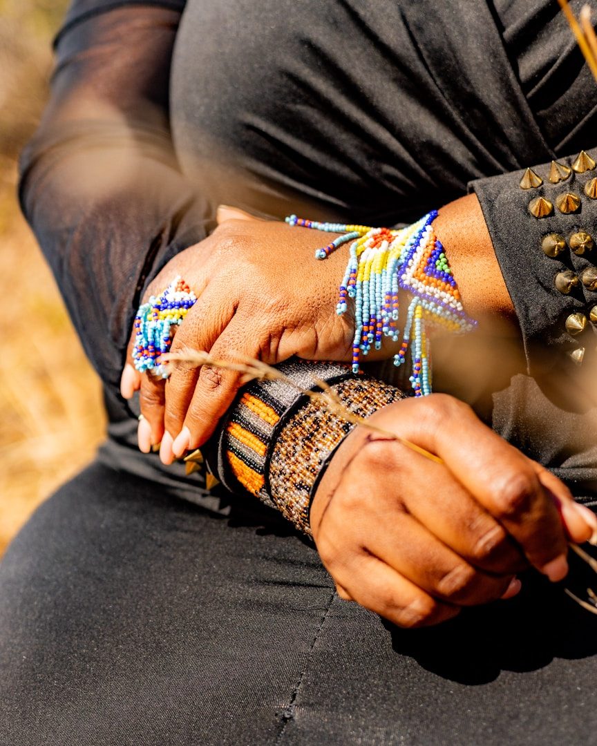 Hände mit bunten Armbändern und Schmuck, auf einem dunklen Kleid abgebildet.