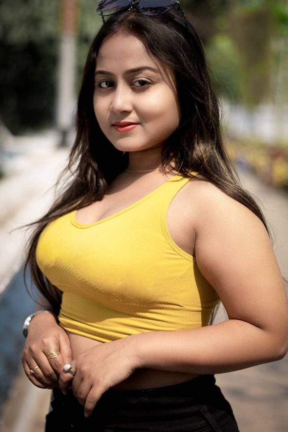 Junge Frau mit langen Haaren, trägt ein gelbes Top und lächelt, im Freien fotografiert.