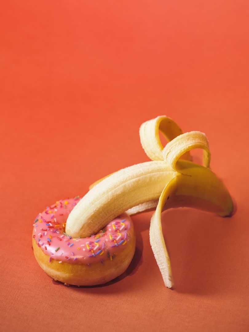 Eine Banane liegt auf einem bunten Donut mit pinkem Zuckerguss und Streuseln.