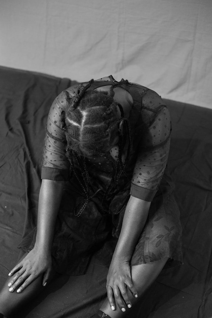 Eine Person in Schwarzweiß sitzt nachdenklich und gekrümmt auf einem dunklen Untergrund.