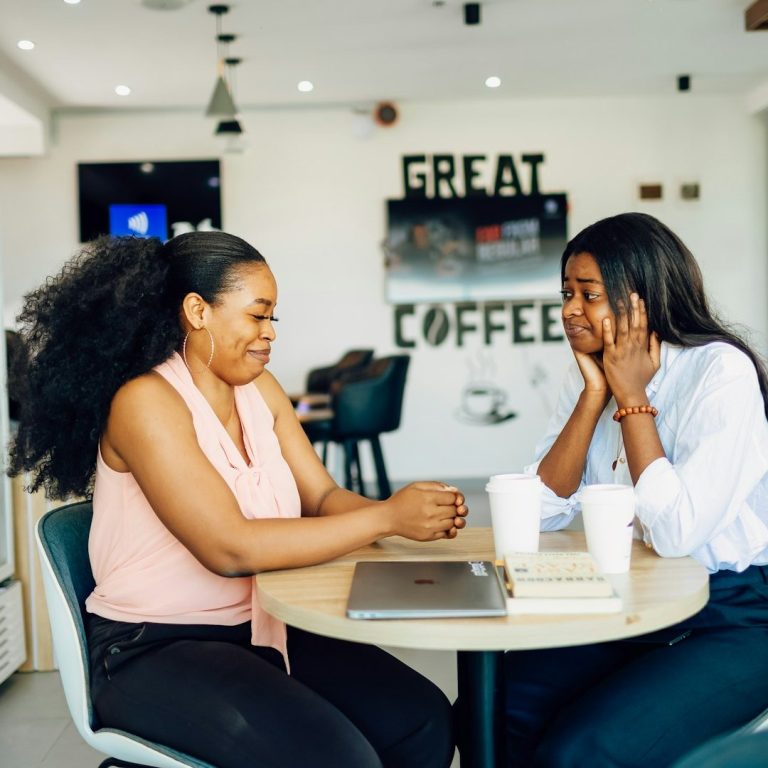 Zwei Frauen sitzen an einem Tisch, lachen und unterhalten sich in einem Café.